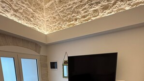 A room with a large flat-screen TV on a white cabinet, a sliding glass door, and a textured ceiling. - Mediterranean Deluxe Stone House (Molfetta)