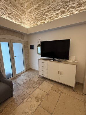 A room with a large flat-screen TV on a white cabinet, a sliding glass door, and a textured ceiling. - Mediterranean Deluxe Stone House (Molfetta)
