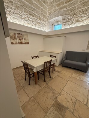 A dining area with a table and chairs, a sofa, and a stone-tiled floor. - Mediterranean Deluxe Stone House (Molfetta)