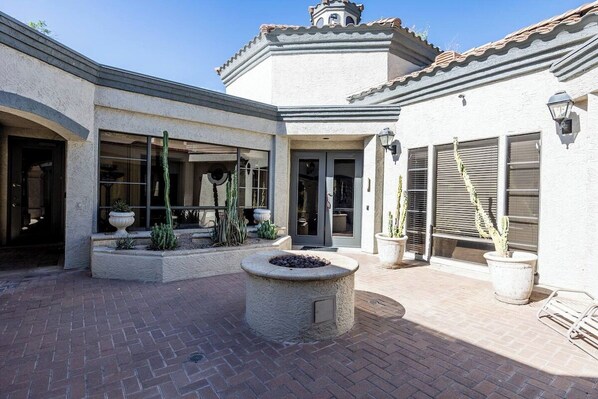 A courtyard with a fire pit, potted plants, and a building with a tiled roof and stucco walls. - Scottsdale Retreat: Pool & Sauna (Scottsdale)