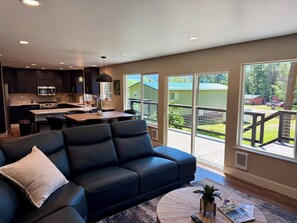 A modern kitchen with dark cabinets, a central island, and a dining area with a black leather couch and a coffee table.