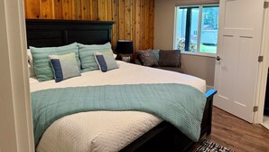 Une chambre à coucher comprenant un lit, un mur recouvert de panneaux en bois, un ventilateur de plafond, une fenêtre et une porte.