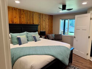 A bedroom with a bed, wooden panel wall, ceiling fan, window, and door.