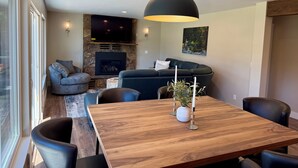 Un salon moderne avec une cheminée en pierre, un téléviseur à écran plat, un canapé foncé et un coin repas comprenant une table et des chaises en bois.
