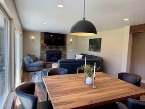 A modern living room with a stone fireplace, a flat-screen TV, a dark sofa, and a dining area with a wooden table and chairs.