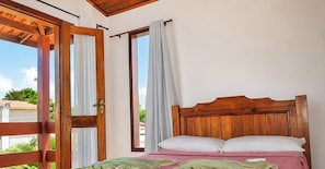 A bedroom with a wooden headboard, a bed with white pillows, and a view through an open door. - Casa Taperapua c Piscina e Sinuca -PS-BA (Porto Seguro)