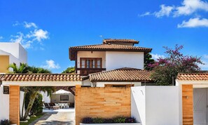 A residential building with a tiled roof, a wooden balcony, and a brick wall. - Casa Taperapua c Piscina e Sinuca -PS-BA (Porto Seguro)
