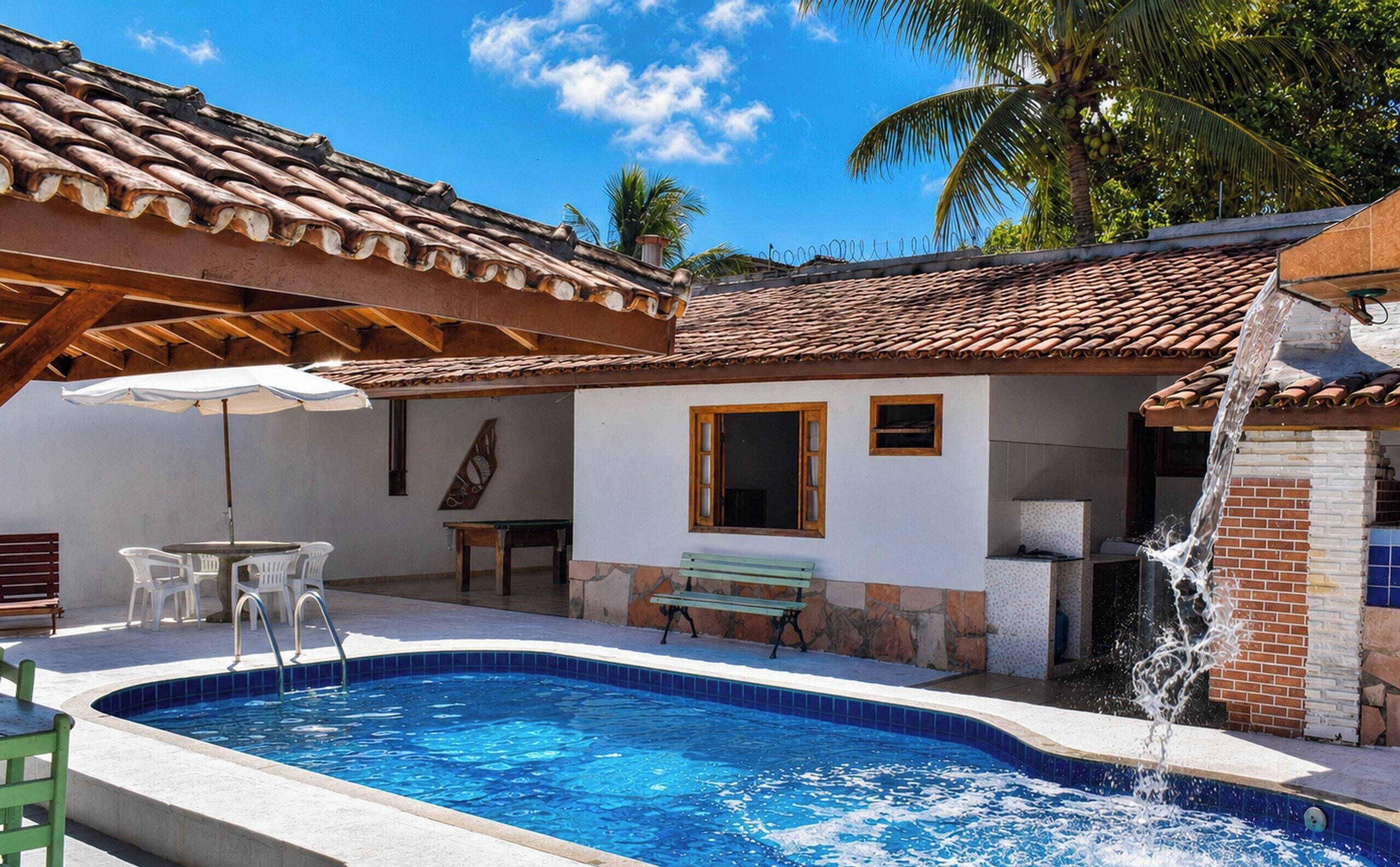 A swimming pool with a tiled edge, a wooden pergola, a bench, and a small table with chairs.