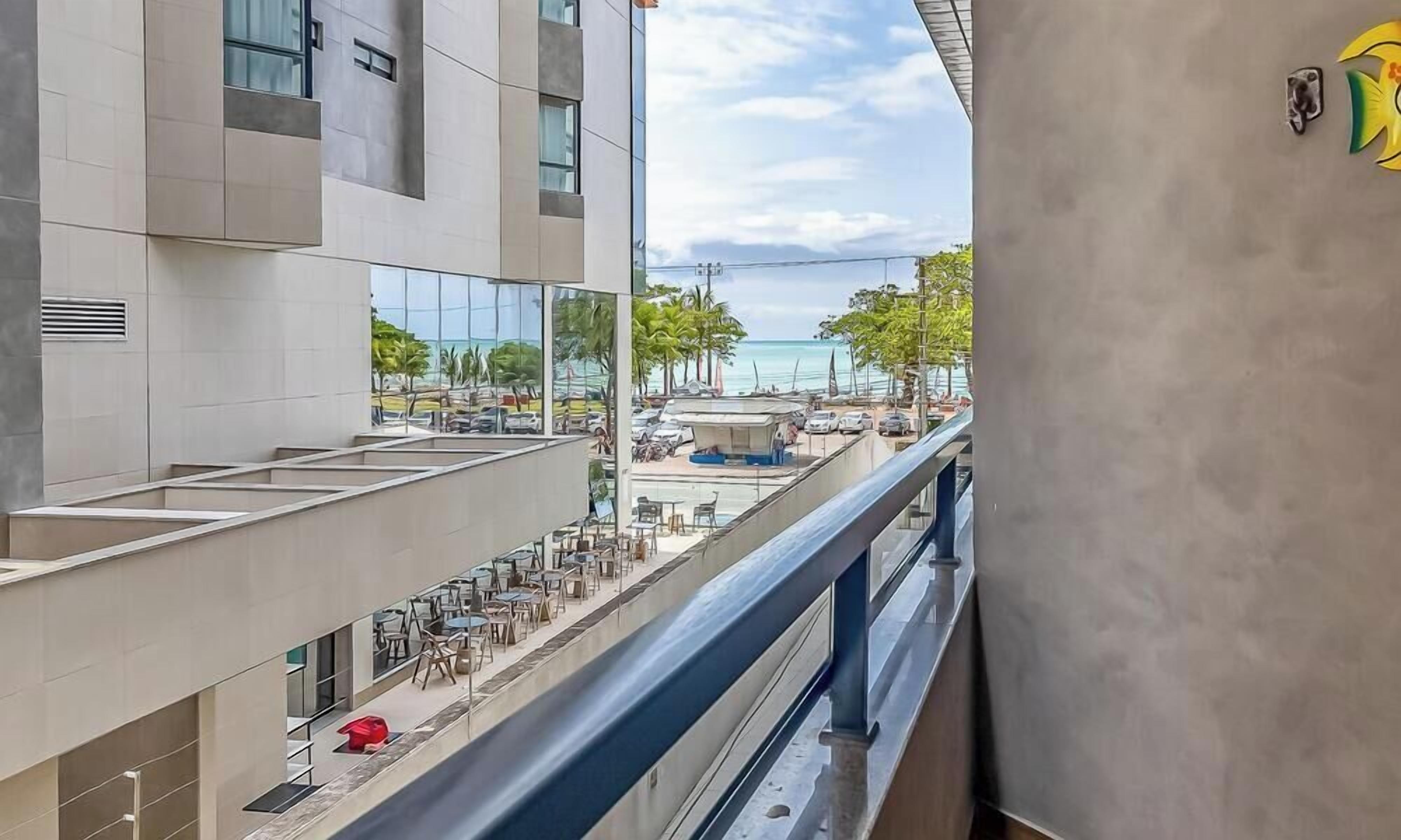 A modern building with a balcony overlooking a beach area, featuring outdoor seating and a view of the sea.