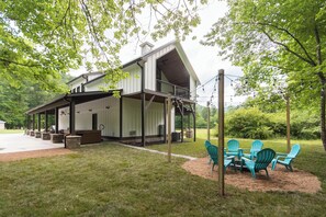 Une maison moderne à deux étages, dotée d’un patio couvert, d’un espace salon extérieur et offrant une vue sur la verdure environnante.