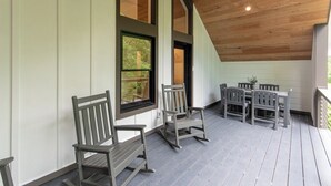 A covered porch with wooden flooring, a dining table with chairs, and large windows. - Luxury Barndominium w/ Hot Tub, Wifi & Trout Fishing (Franklin)