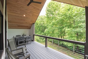 Eine Holzterrasse mit Tisch und Stühlen, einem Deckenventilator und Blick auf einen Wald.