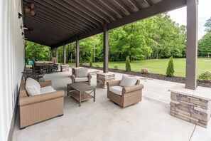Eine Terrassengrundstück mit Korbmöbeln, einem Kamin aus Stein und Blick auf eine grüne Landschaft.