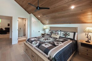 Ein Schlafzimmer mit Holzboden, einem Bett mit Steppdecke, zwei Nachttischen, einer Lampe und einer Tür zu einem anderen Raum.