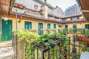 Ein Innenhof mit einem Metallzaun, Kübelpflanzen und einem Gebäude mit grünen Fensterläden.