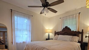 A bedroom with a bed, a ceiling fan, a nightstand, a lamp, and a window with curtains.