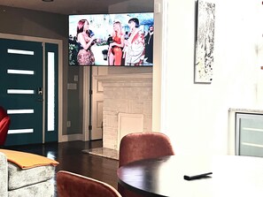 A room with a television mounted on the wall, a fireplace, and a dining area with chairs and a table. - 3-bedroom house in charming Atlanta with cool AC comfort (Atlanta)