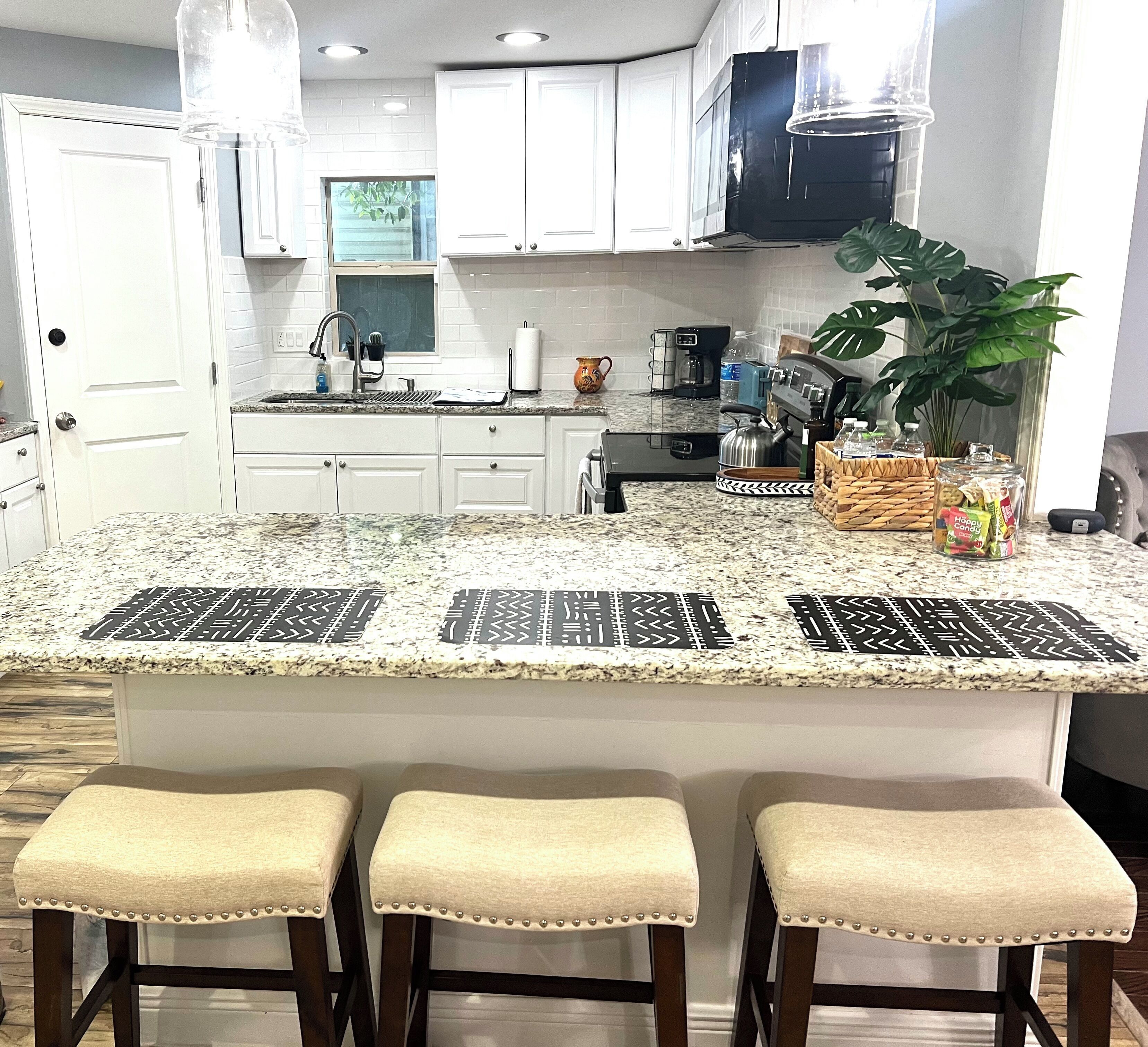 A kitchen with white cabinets, a granite countertop, and three bar stools.
