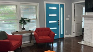 Un salon avec un fauteuil rouge, un canapé gris et un tapis orange.