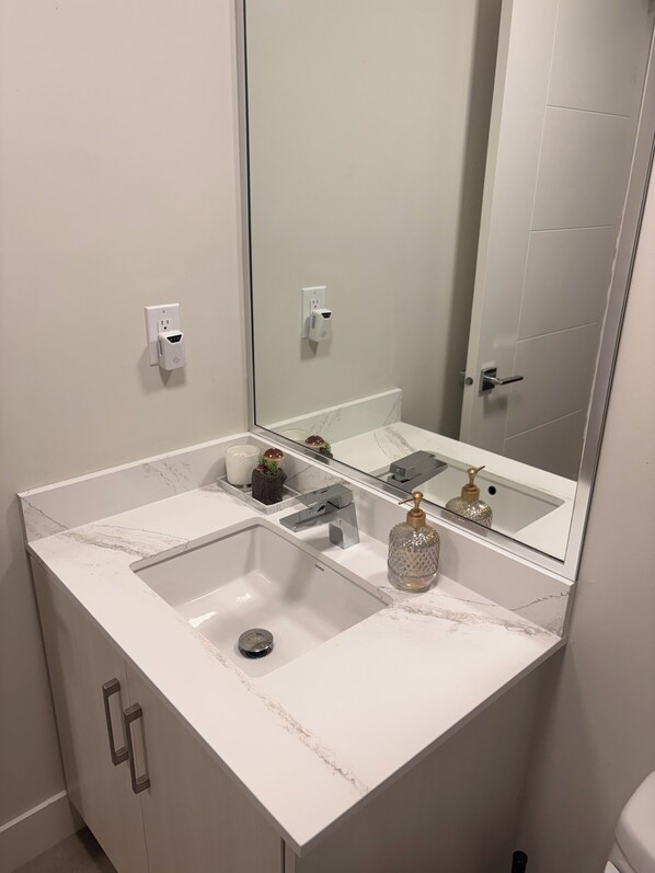 A bathroom with a white marble sink, a mirror, a door, and a wall-mounted outlet. - Terrific 2-bedroom guest suite in Burnaby (Burnaby)