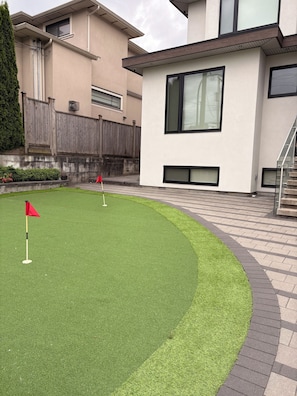 A modern building with a flat roof, large windows, and a paved patio area with artificial grass and a red flag.