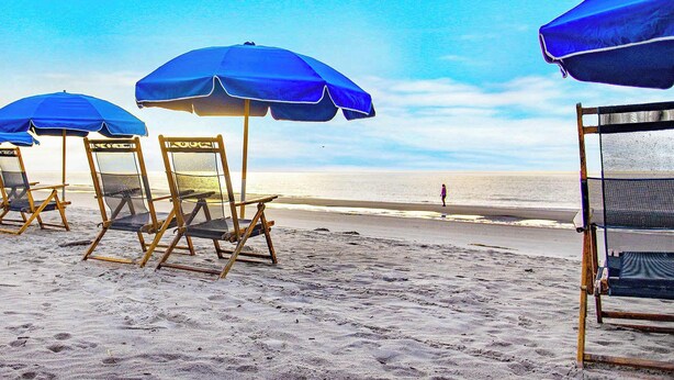 Une plage avec des parasols bleus et des chaises en bois.
