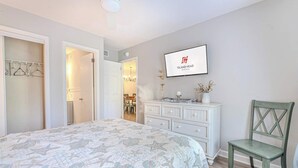 Une chambre à coucher comprenant un lit, une commode, une chaise, un téléviseur et un couloir menant à une salle à manger.