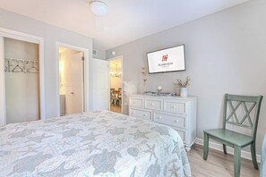 A bedroom with a bed, a dresser, a chair, a TV, and a hallway leading to a dining area. - Beachfront Resort Villa Pool, Steps to the Sand (Hilton Head Island)