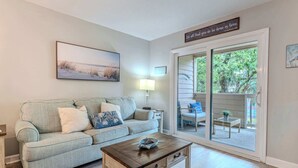Un salon avec un canapé, une table basse et un tableau au mur. Une porte-fenêtre coulissante donne sur un espace extérieur aménagé avec du mobilier.