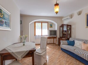 Una sala de estar con un sofá, un televisor, una mesa de comedor con mantel de encaje y un aparador decorativo.