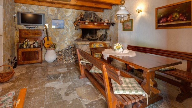 A rustic interior with a stone fireplace, wooden beams, a television, a guitar, and a dining table with benches.