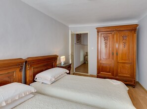 A bedroom with two beds, a wooden wardrobe, a nightstand with a lamp, and a door leading to another room. - Holiday Home with Sea View (Mali Losinj)
