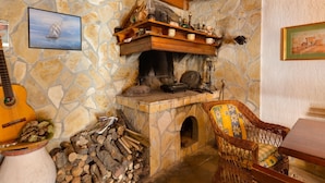 A rustic stone fireplace with a wooden mantel, a guitar, and a wicker chair.