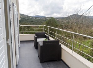 A balcony with wicker furniture, a metal railing, and a view of green hills. - Four Bedroom Villa with Terrace (Ston)
