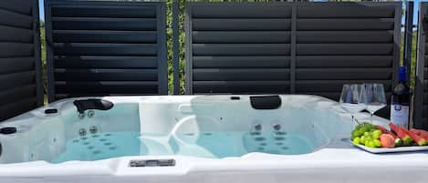A hot tub with a table beside it, under an umbrella, surrounded by a fence.