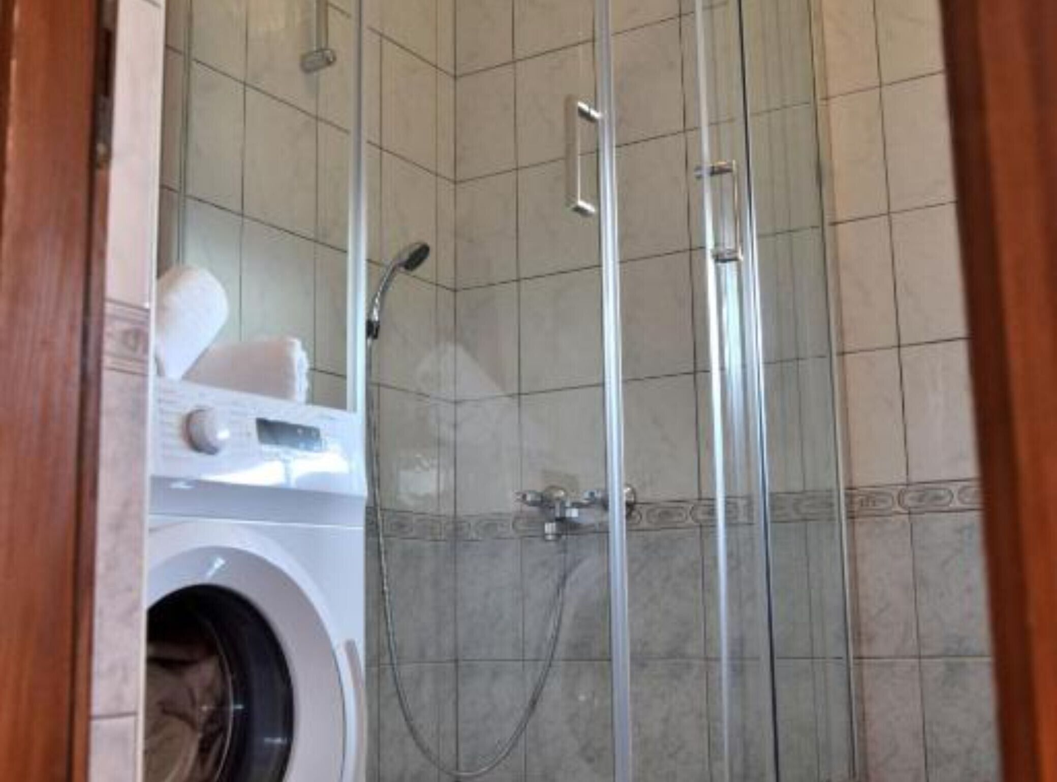 Une salle de bain avec une douche à parois de verre, un lave-linge et des murs carrelés.