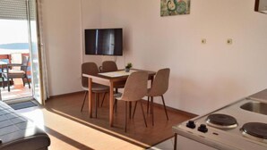 A dining area with a table and chairs, a television on the wall, and a kitchen with a stove. - two bedroom apartment with terrace and balcony (Rab)