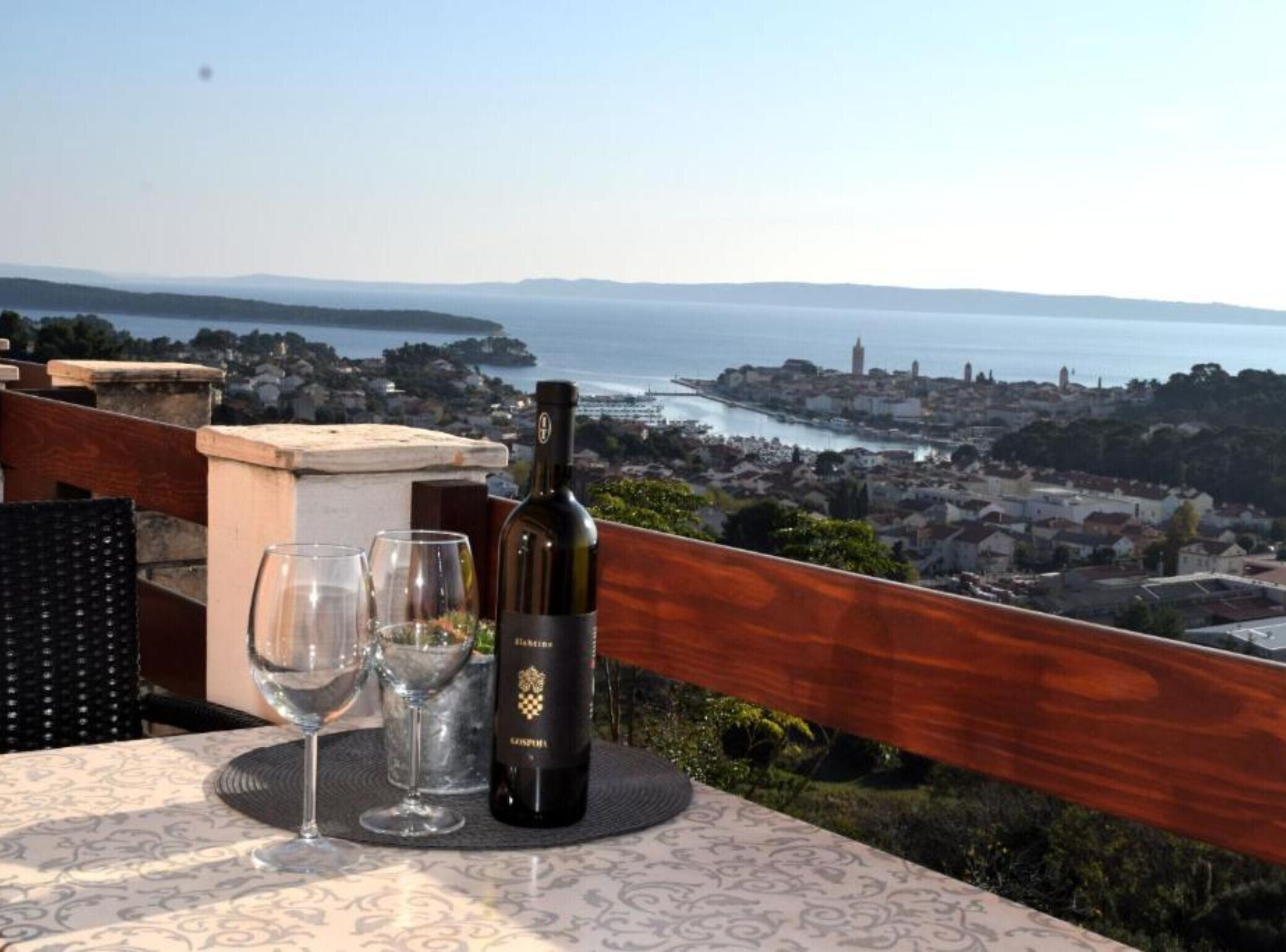 A table with a bottle of wine and glasses, overlooking a coastal cityscape.