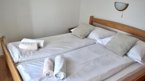 A double bed with white linens and two rolled towels, a wooden headboard, and a wall-mounted light fixture. - two bedroom apartment with terrace and balcony (Rab)