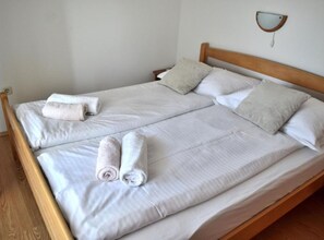 Ein Doppelbett mit weißen Leinen und zwei zusammengerollten Handtüchern, ein Holz-Kopfteil und eine wandmontierte Leuchte.
