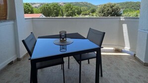 Un balcon avec une table et des chaises, un verre, et une vue sur la verdure et les collines.