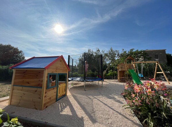 A wooden playhouse, a trampoline, and a wooden swing set in a garden.