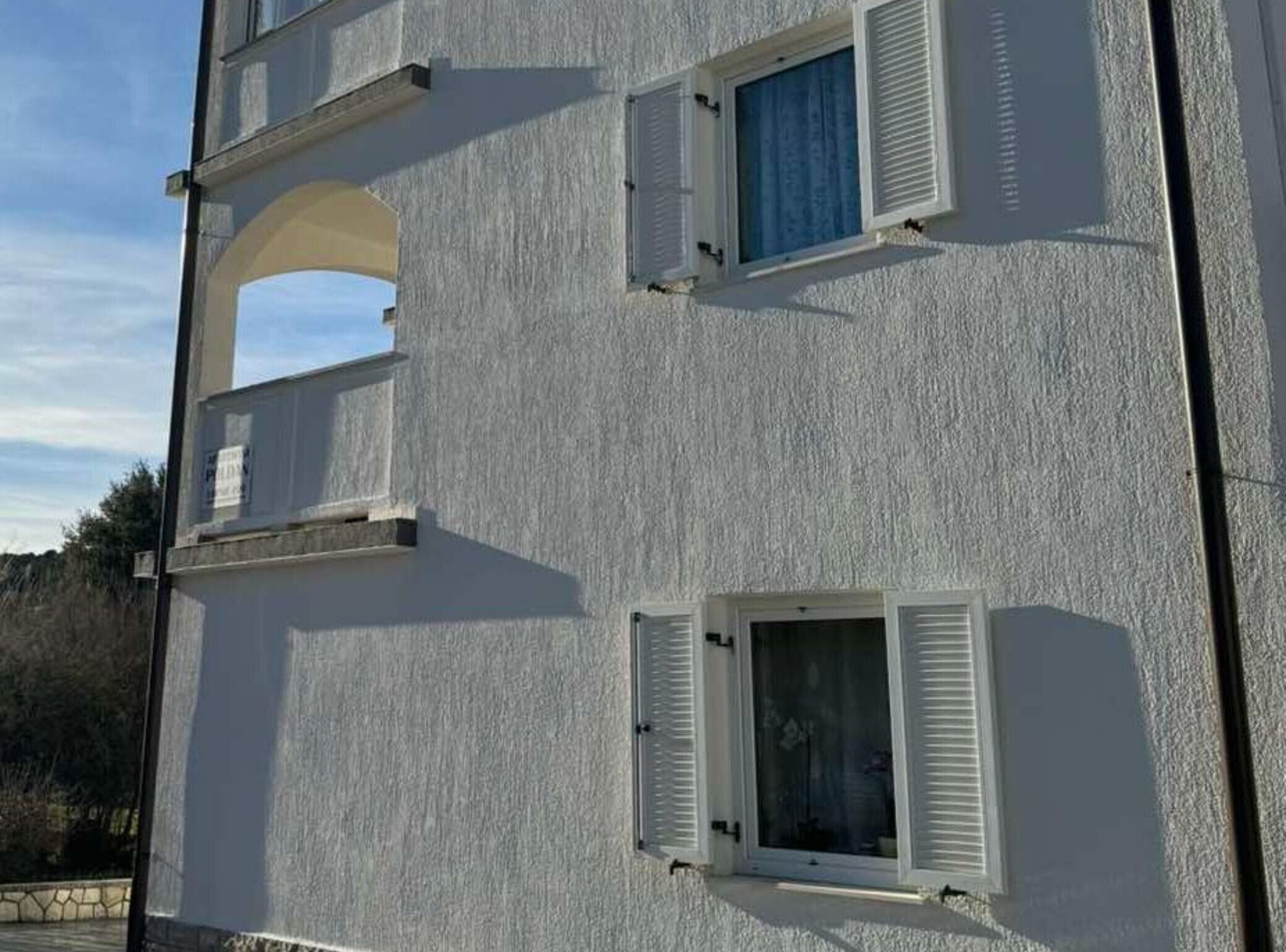 A multi-story building with white exterior walls and shutters on the windows.