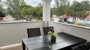 Un balcon avec une table et des chaises, un pot de fleurs et une vue sur les arbres et les bâtiments.
