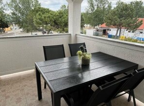 A balcony with a table and chairs, a potted plant, and a view of trees and buildings. - Comfort Two Bedroom Apartment with Balcony (Rab)