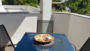 A balcony with a table and chairs, a satellite dish, and a view of trees and houses. - Two Bedroom Apartment with Balcony (Rab)