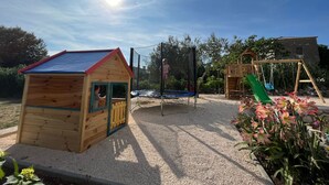 A wooden playhouse, a trampoline, and a wooden swing set in a garden. - Two Bedroom Apartment with Balcony (Rab)