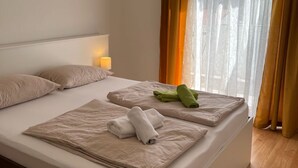A hotel room with a bed, pillows, a lamp, and a window with curtains. - Two Bedroom Apartment with Balcony (Rab)
