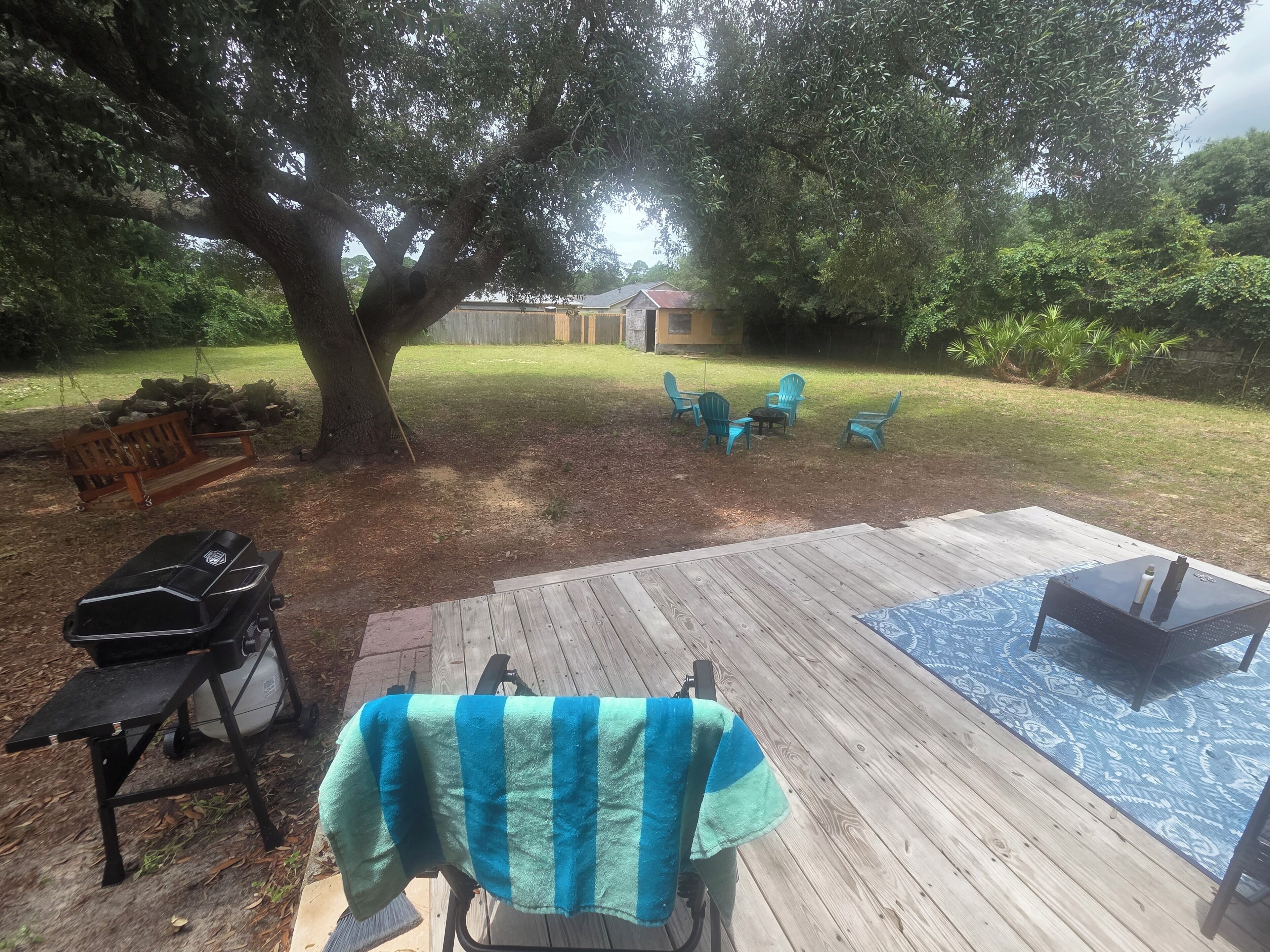 A backyard with a wooden deck, outdoor furniture, a grill, and a tree providing shade.