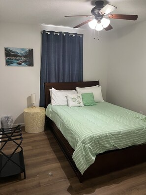 Een slaapkamer met een bed, een plafondventilator, een aan de muur bevestigd schilderij, een rond bijzettafeltje en een stoel.